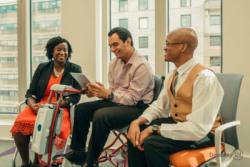 Three people sitting together and looking at an iPad Credit: Disability:IN